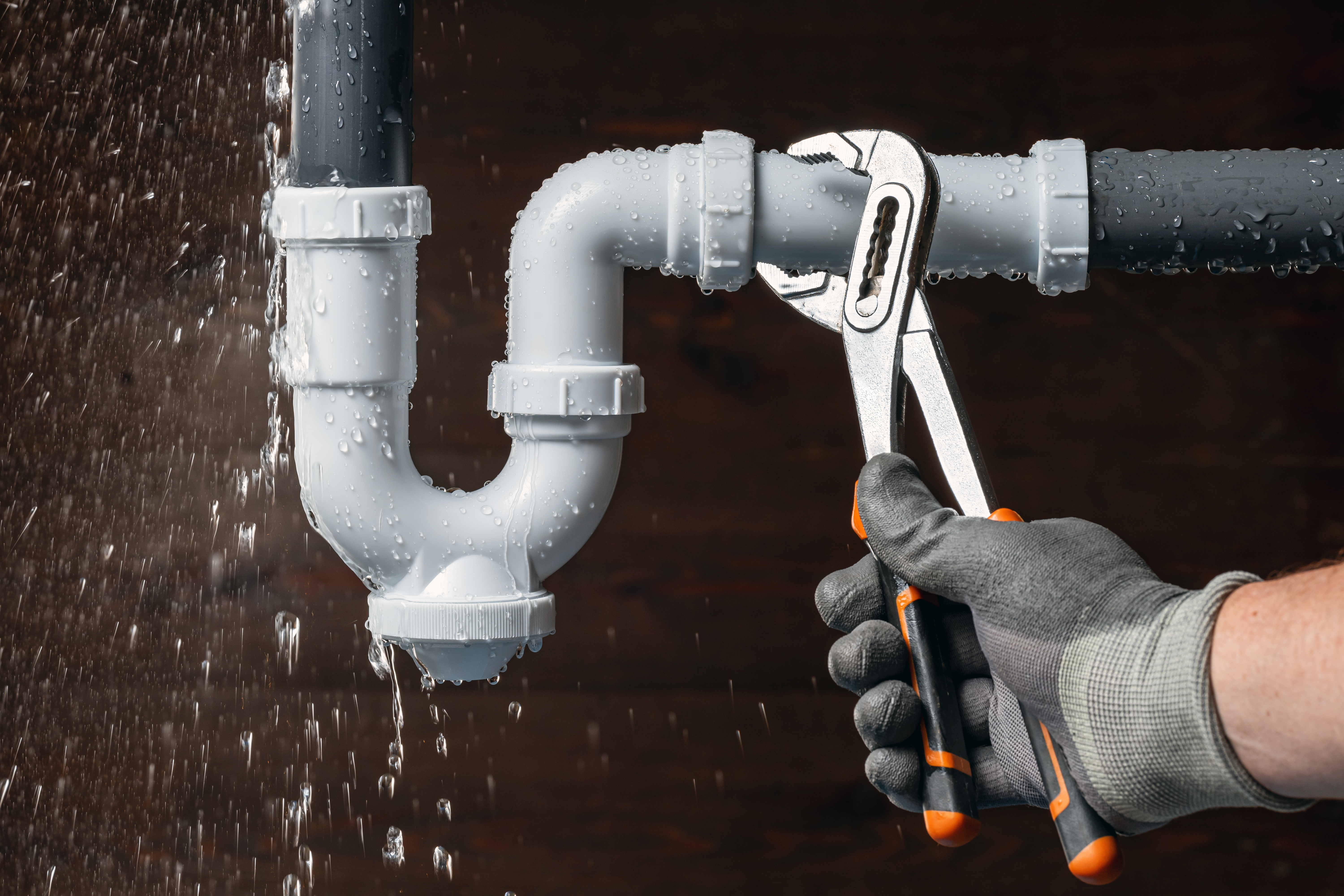 Close up of a plumber hand fixing a water leak in a sink drain siphon pipe with an adjustable pliers. Home insurance for emergency plumbing breakdowns repair.